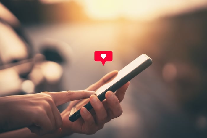 Hand tapping smartphone with heart icon coming out. 