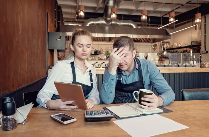 Two restaurant workers frown at financial papers at a table.
