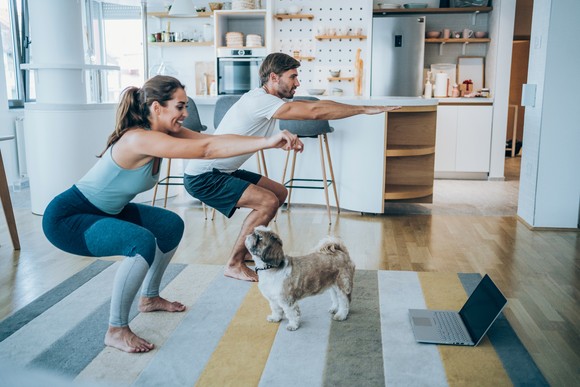 A couple working out with their dog curiously watching.