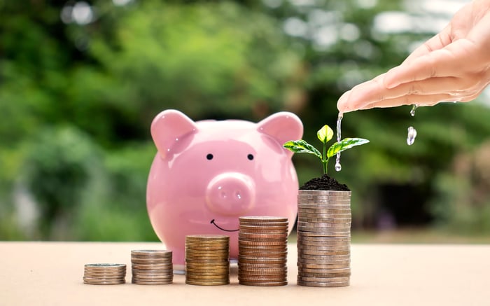 Stacks of coins in front of a piggy bank with a green shoot emerging to represent growth.