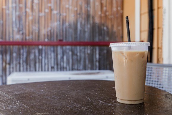 A cold coffee beverage in a takeaway container sitting on a table.