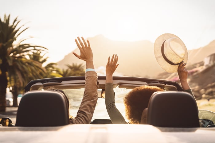 Two people raise their arms in a convertible.