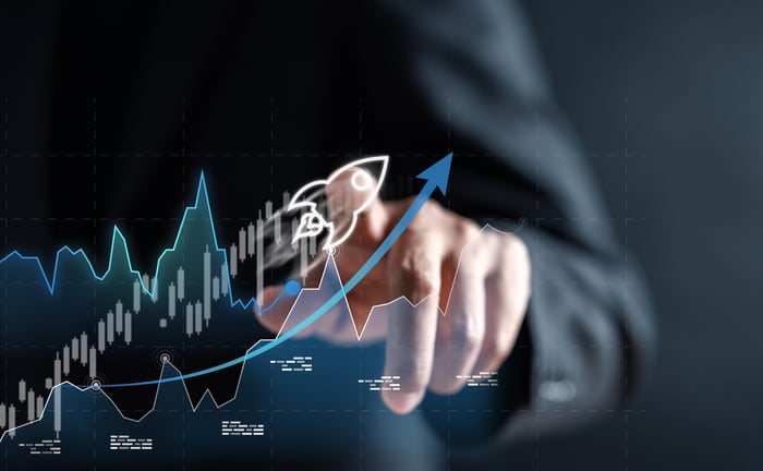 A finger pointing to a drawing of a rocket overlaid on a line and stock chart trending upward.