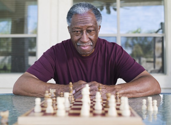 Elderly man carefully studying a chess board. 