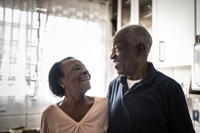 Older couple standing in their kitchen, smiling broadly at each other. 