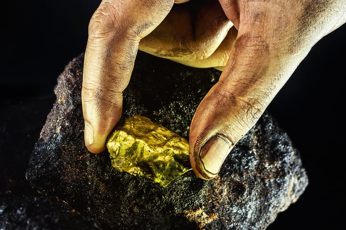 Someone's hand holding a gold nugget embedded in a rock. 