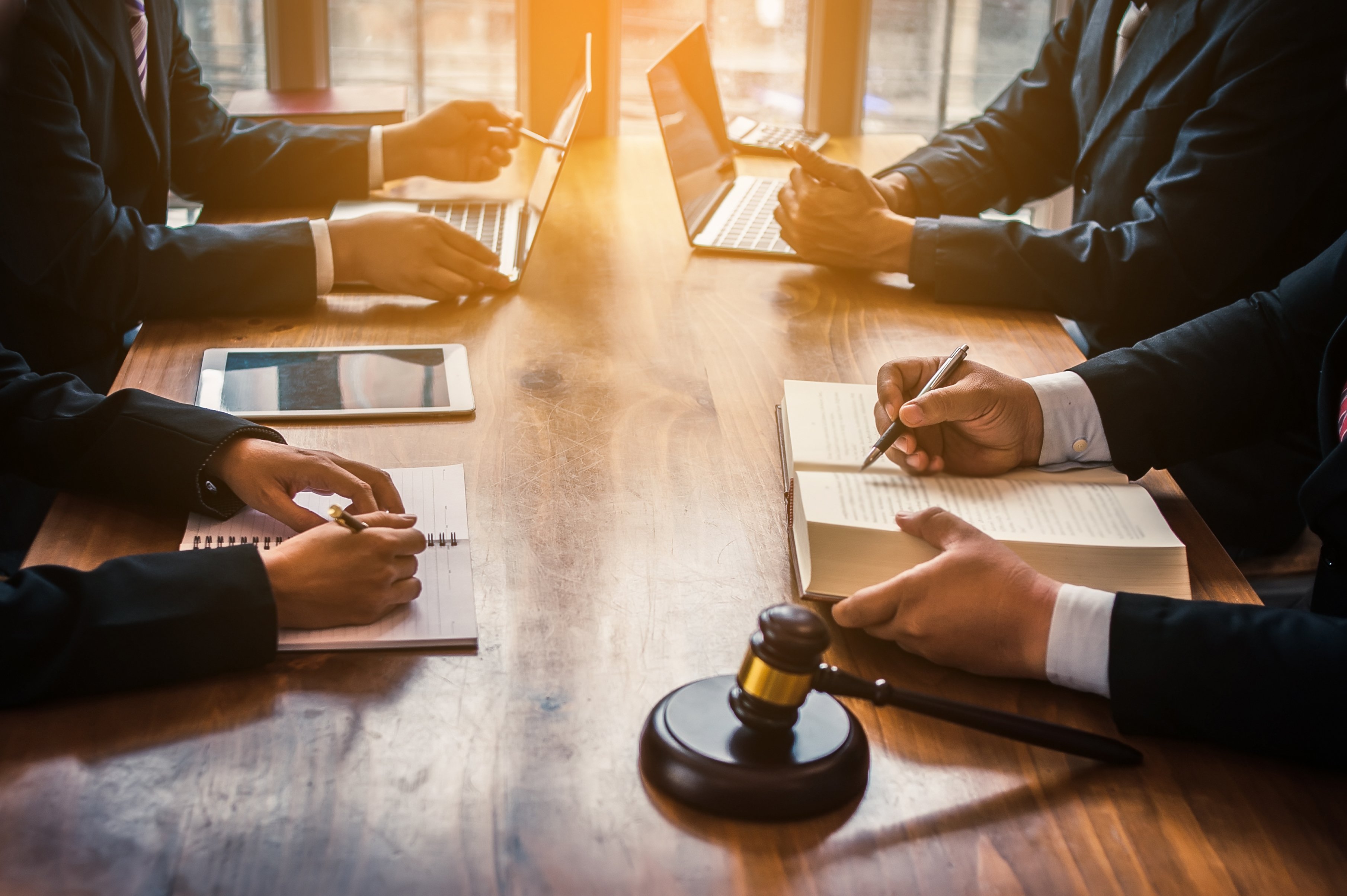 Lawyers and a judge sit around a wooden table with a law book and gavel out. 