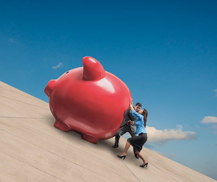 Two people pushing a giant piggy bank up an incline.