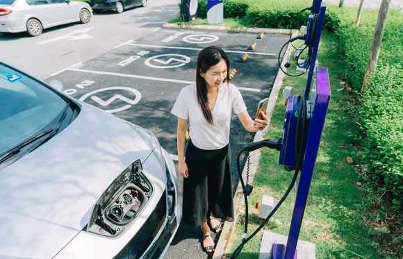 A person checking a display at an electric-vehicle charging station with phone to charge car. 