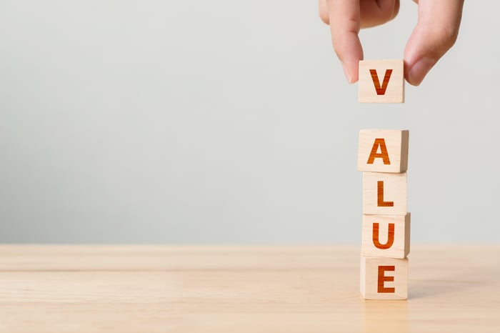 Fingers placing a wooden block with "V" displayed on top of other blocks to spell the word "VALUE."