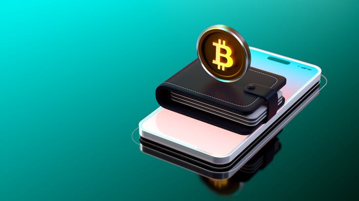 A Bitcoin stands on top of a wallet that's itself resting on top of a cell phone.