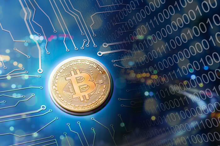 A Bitcoin rests at the center of a circuit board, with computer code flowing toward it.