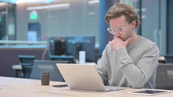 A person sitting at a table looking at a laptop.