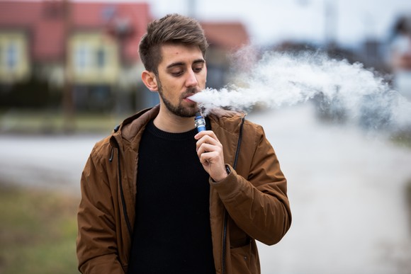 A man walking and using an electronic vaping device. 