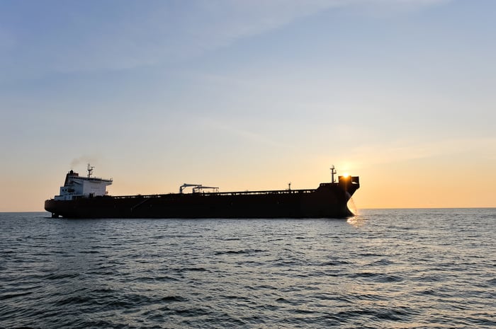 Oil tanker at sea with sun low on horizon.