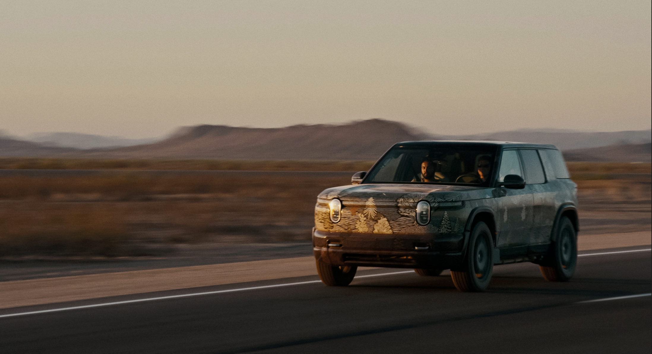 Rivian R1S with forest paint wrap driving down scenic highway.