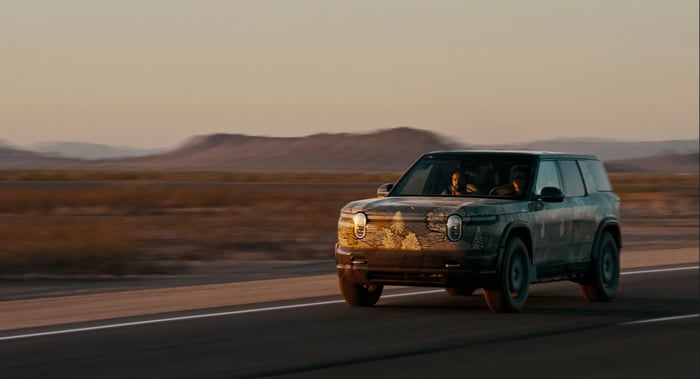 Rivian R1S with forest paint wrap driving down scenic highway.