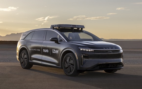 A Lucid Gravity electric SUV with Nuro and Uber logos on its side and visible self-driving sensor hardware, in a desert setting. 