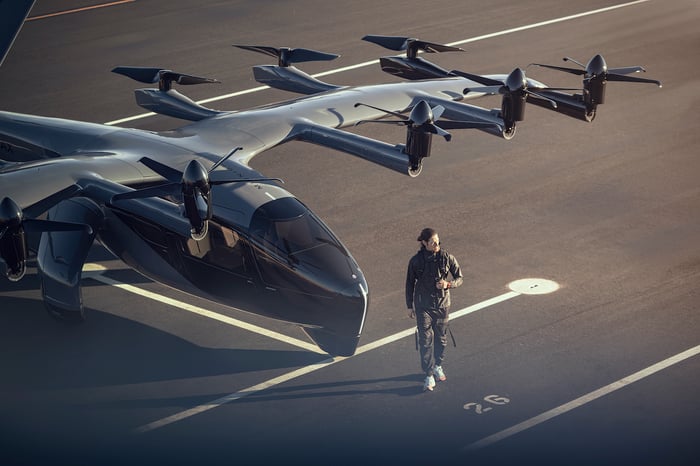 A person walks on the tarmac next to an Archer Aviation Midnight model aircraft