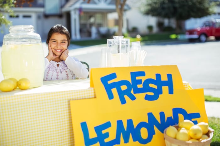 A smiling child running a lemonade stand.