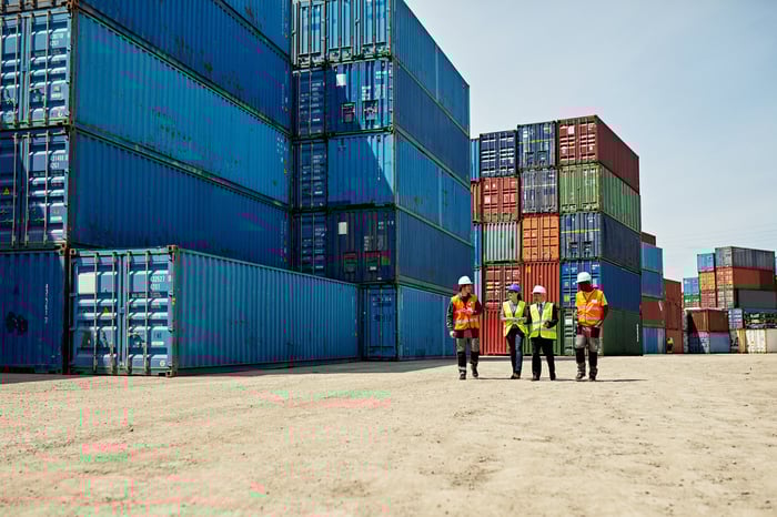 Shipping containers stacked high with workers below. 