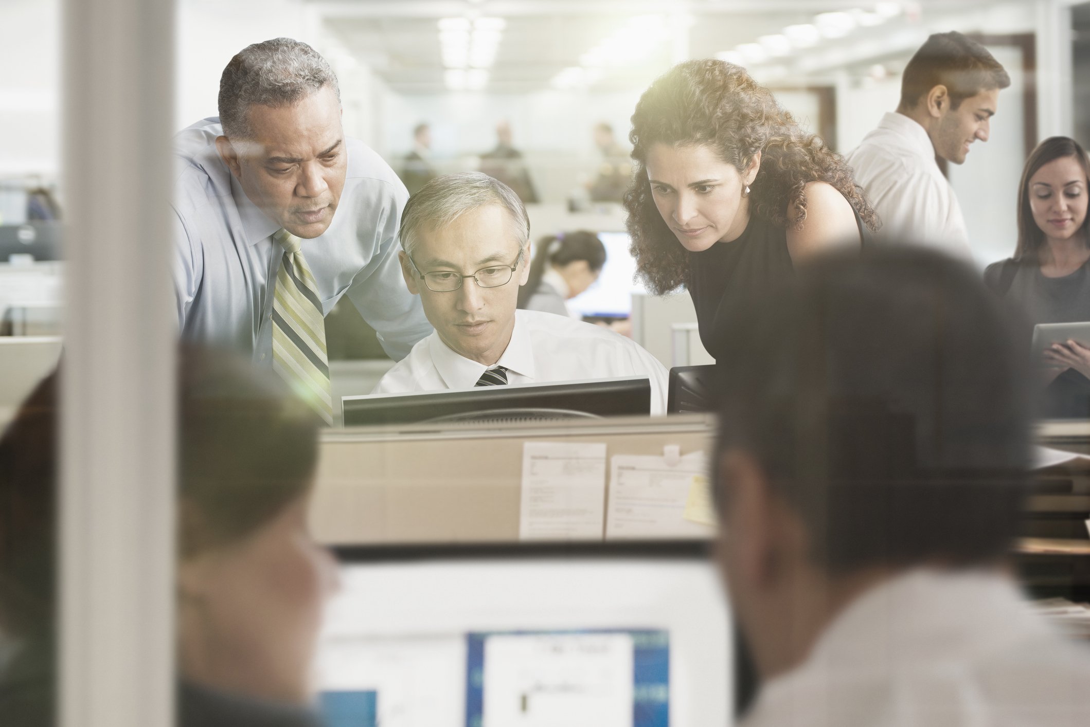People crowding around a computer in an office.