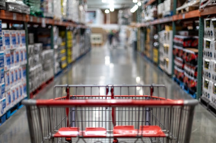 A shopping cart sitting in the aisle of a wholesale store.