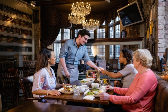 A group of three diners sitting at a table with a waiter standing at one end of the table.  