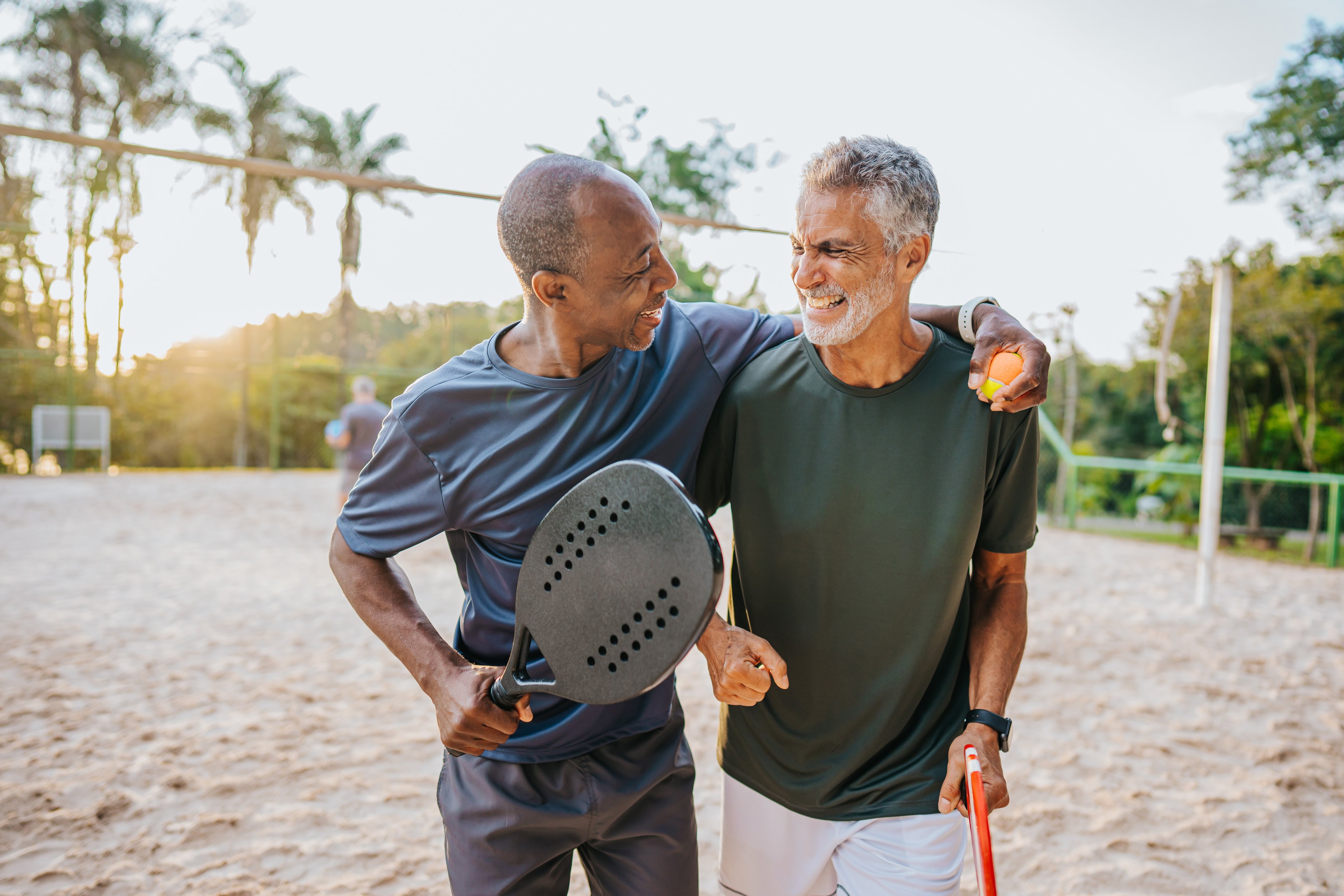 Two people holding rackets or paddles while standing on a sandy court.