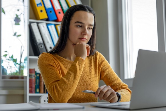 A person with their chin propped on their hand looking at a laptop.