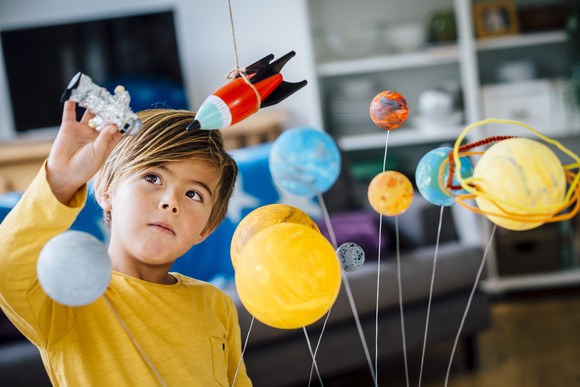 A kid playing with a toy solar system and flying toy rockets around it. 