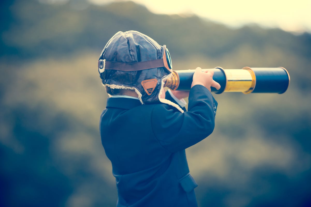 A child wearing an aviator cap looks through a telescope.