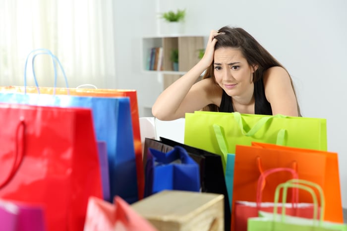 A person frowning at a table full of colorful shopping bags.