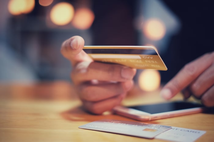 A person holds a credit card and uses a smartphone.