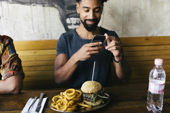 Person photographing a plate with onion rings and a burger on it. 