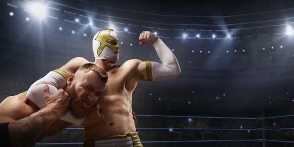 A wrestler in a mask has another in a headlock.