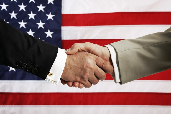 Handshake in front of U.S. flag.
