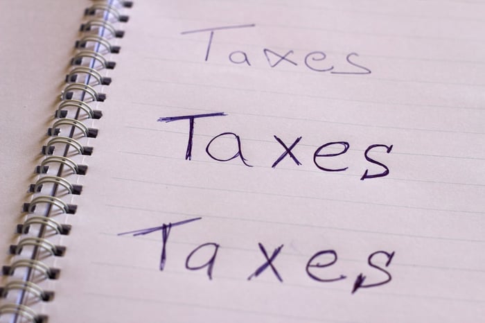 An open spiral notebook with the words, "Taxes, Taxes, Taxes" written in blue ink. 