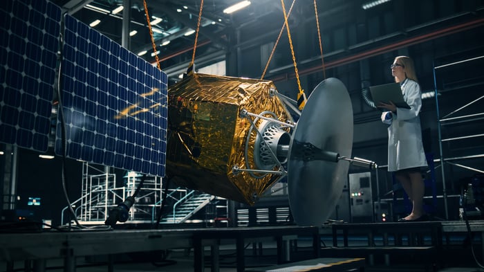 A person in a lab coat working on a satellite in a laboratory. 