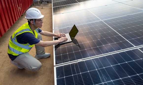 A worker on a laptop next to a solar panel array. 