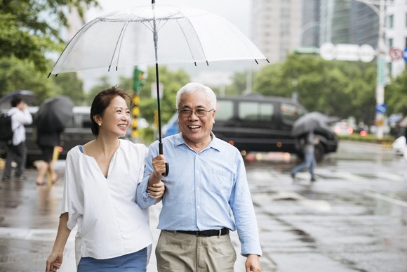 A couple is walking in a city, holding an umbrella and smiling.