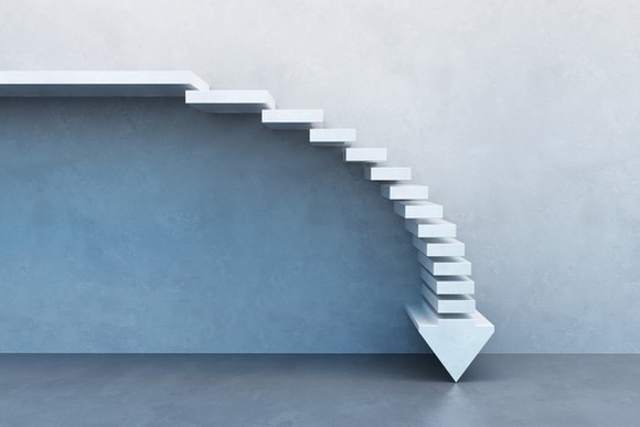 A downward arrow designed as a series of steps against a wall.