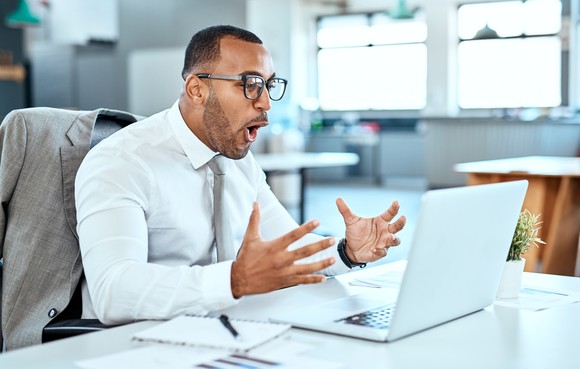 An excited middle-aged man sitting at a desk looking at a laptop.
