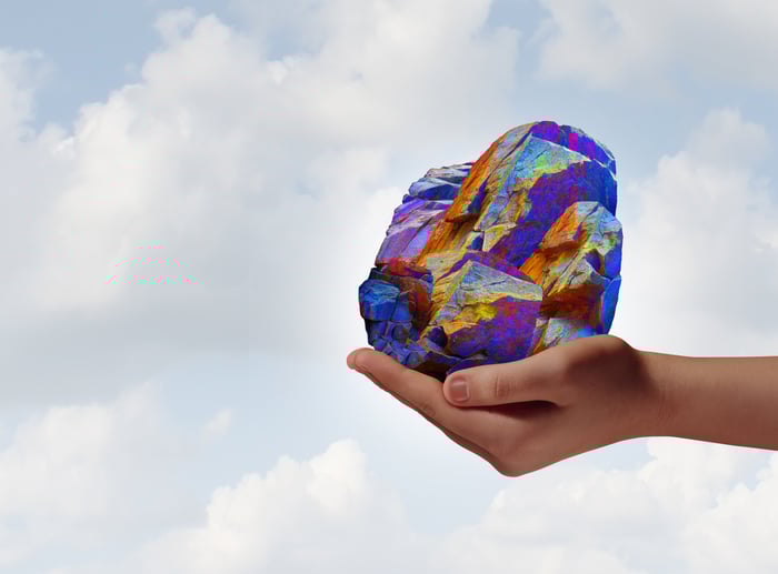 A hand holding a multicolored mineral rock. 
