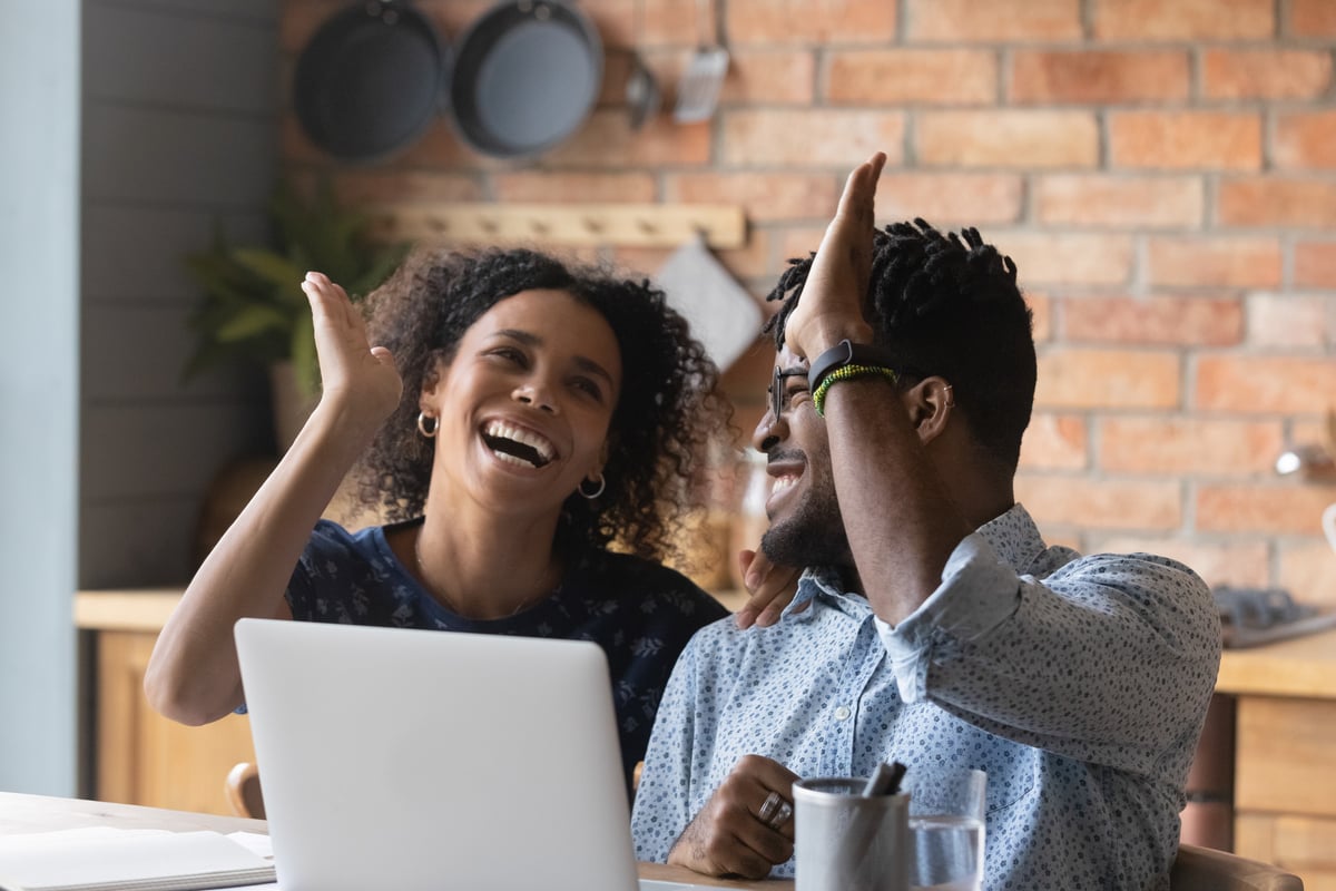 Two investors high five in a kitchen in front of a laptop.
