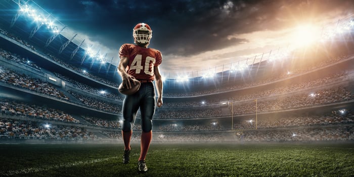 Football player on the field at night clutching a ball.