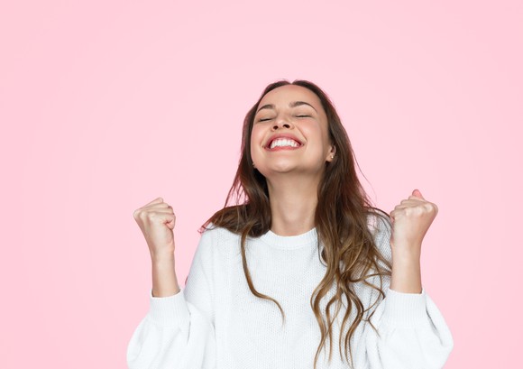 Person celebrates in white clothes against pink background.