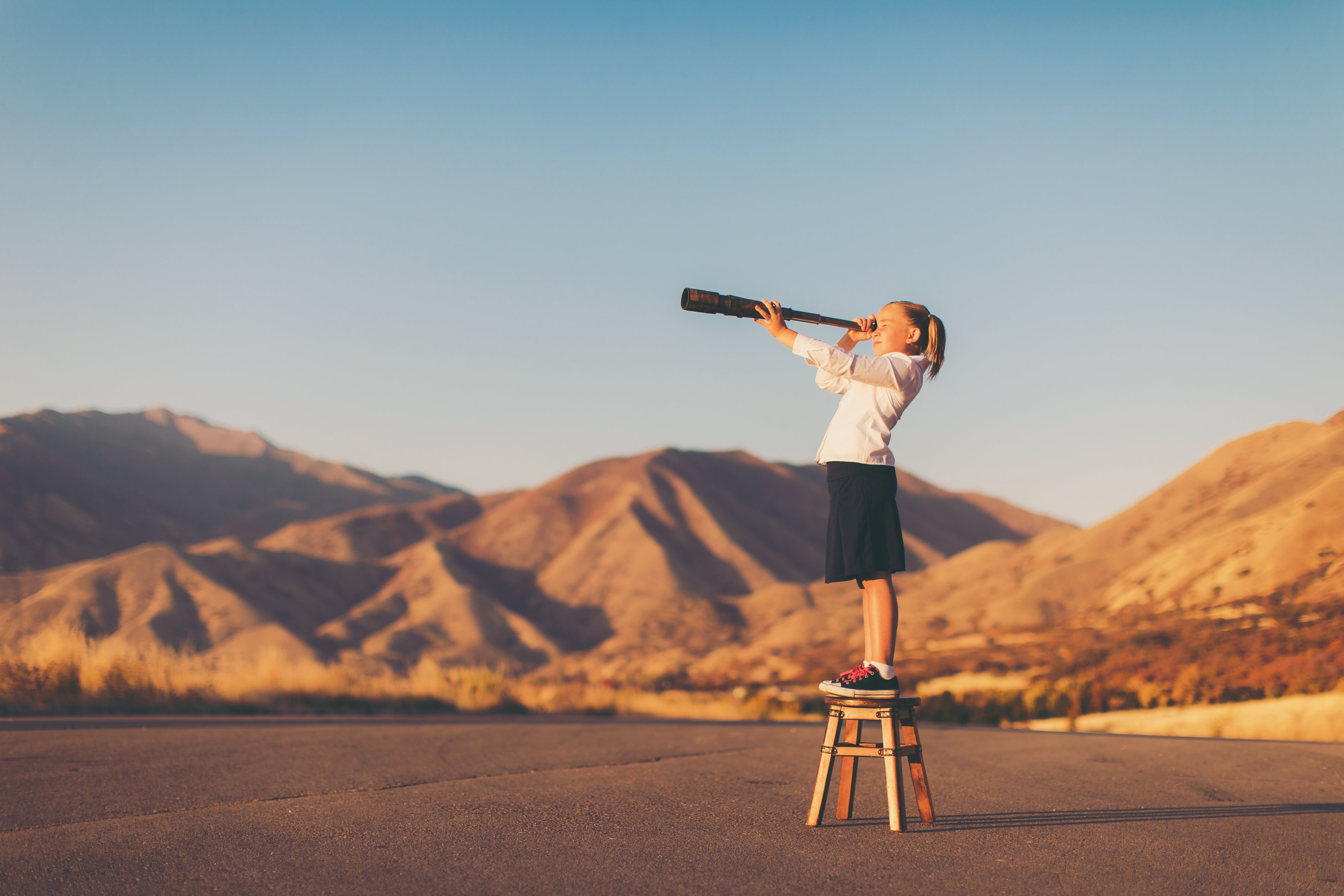 A child looking into the distance through a telescope.