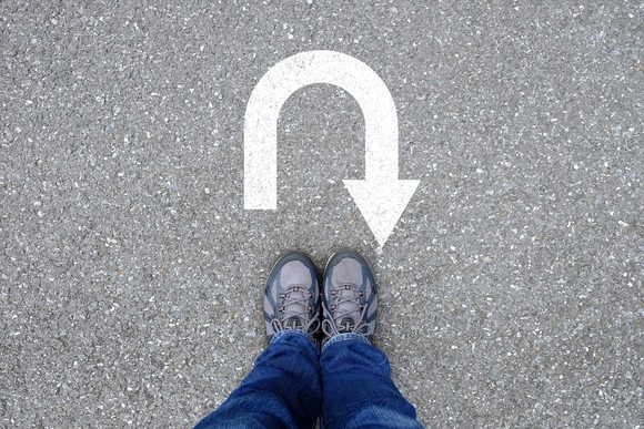 A person standing in front of a U-turn arrow painted on a cement walkway.