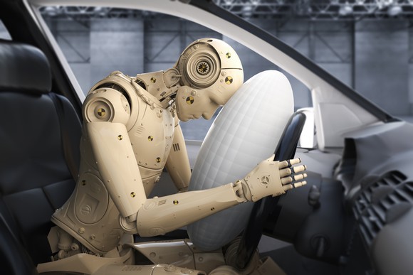 A crash test dummy in the driver's seat of a car with the airbag deployed